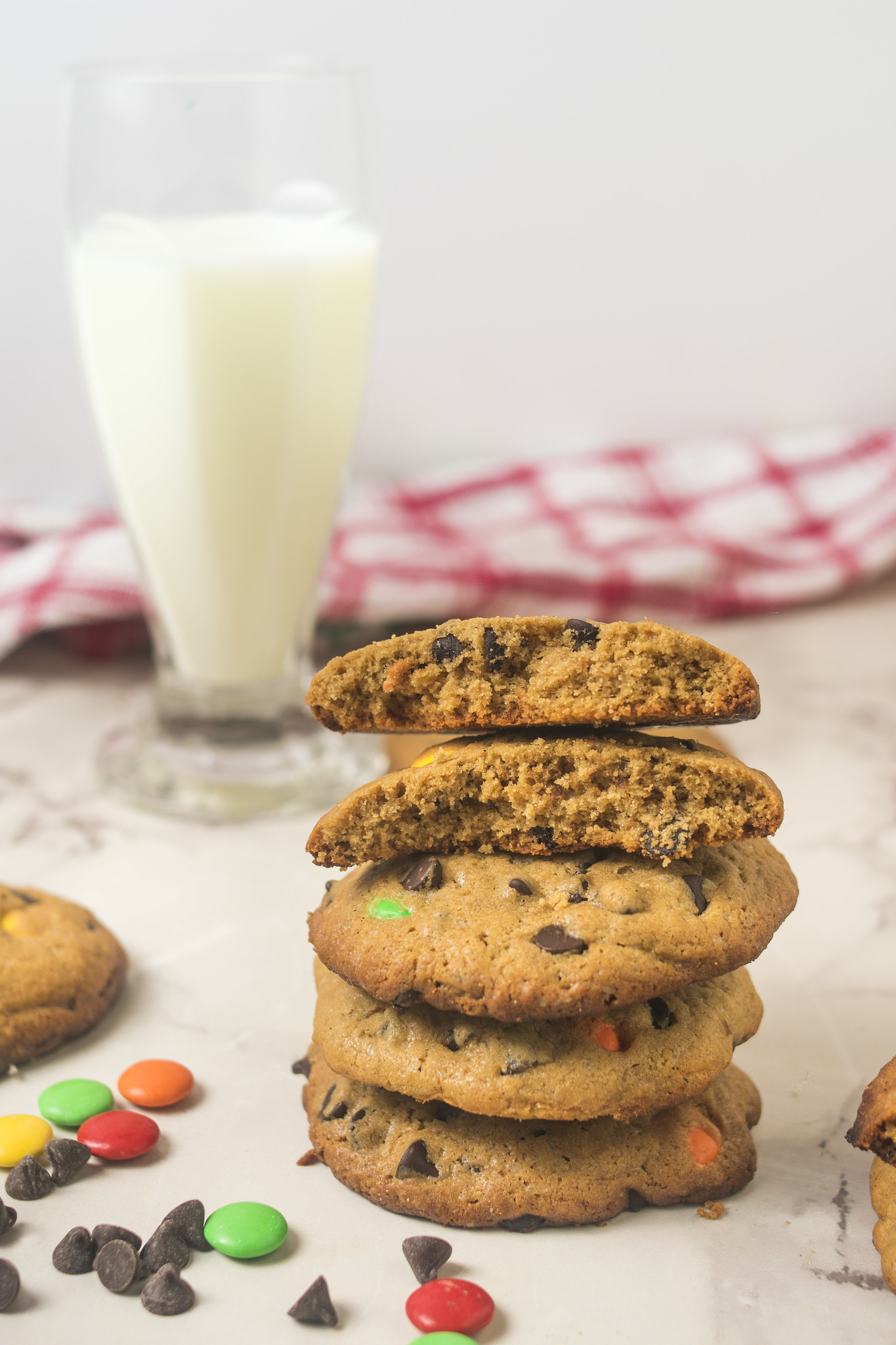 Stack of browned butter chocolate chip cookies with chocolate chips, M&Ms and a glass of milk.